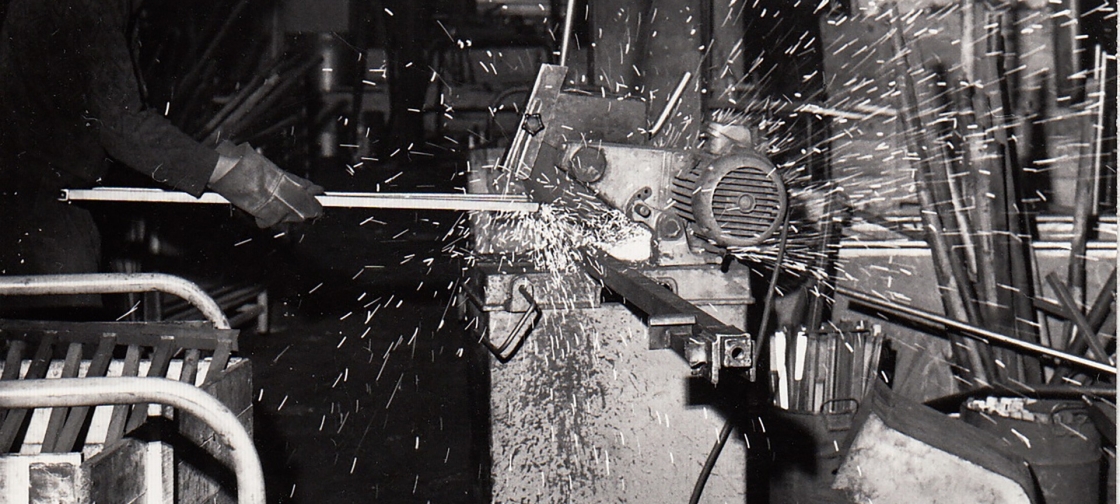 Foto en blanco y negro de un trabajador mecanizando una estantería en los años 70
	                        