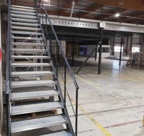 Escalera metálica industrial instalada en un almacén para acceder a una plataforma
			
