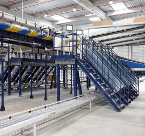 Pasarela con escaleras en un almacén que permite el acceso sobre cintas transportadoras
			