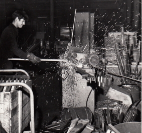 Foto en blanco y negro de un trabajador mecanizando una estantería en los años 70
			