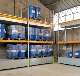 Estanterías pesadas con cubetos de retención utilizadas para almacenar bidones de productos químicos en un hangar
			