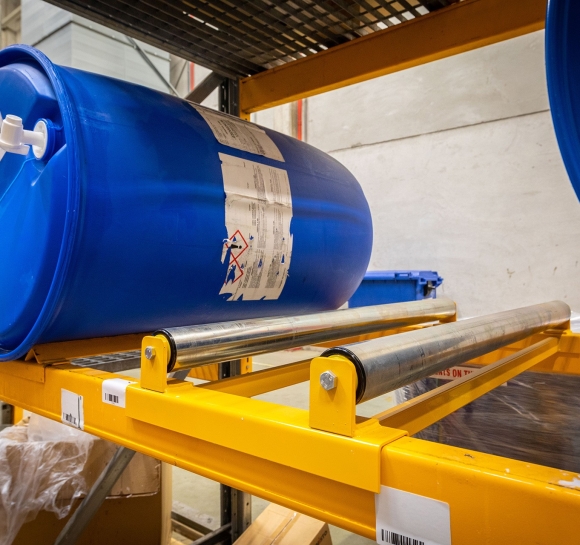 Almacenamiento de bidones de plástico en una estantería industrial equipada con rodillos para hacerlos girar
